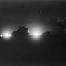 Vehicles silhouetted against the flash of artillery